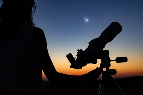 stock photo of person standing next to a telescope under the night sky