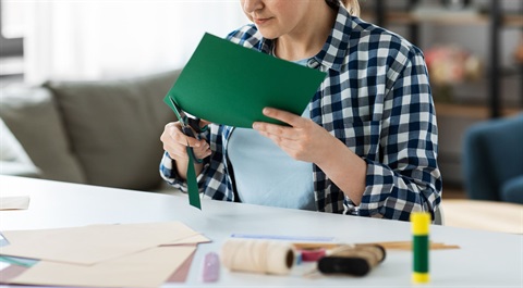 Woman cutting green paper with scissors.