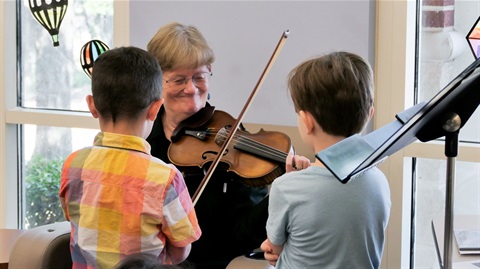 Woman playing violin while two children watch