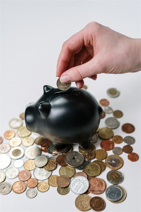 Coins on a table and a hand putting a coin in a piggy bank.