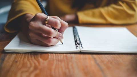 adult using a pen to write in a notebook