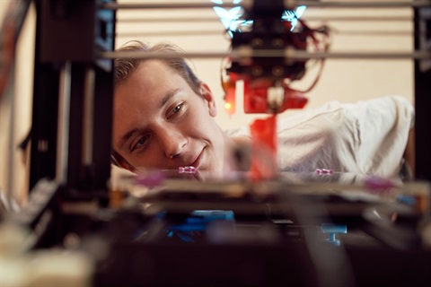 Young man looking at a 3d printer printing something.