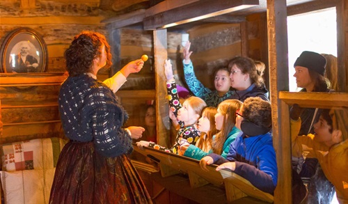 a costumed staff member talks to guests at the Log Cabin Village