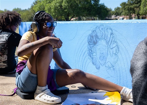 A student sketching her mural onto a wall.